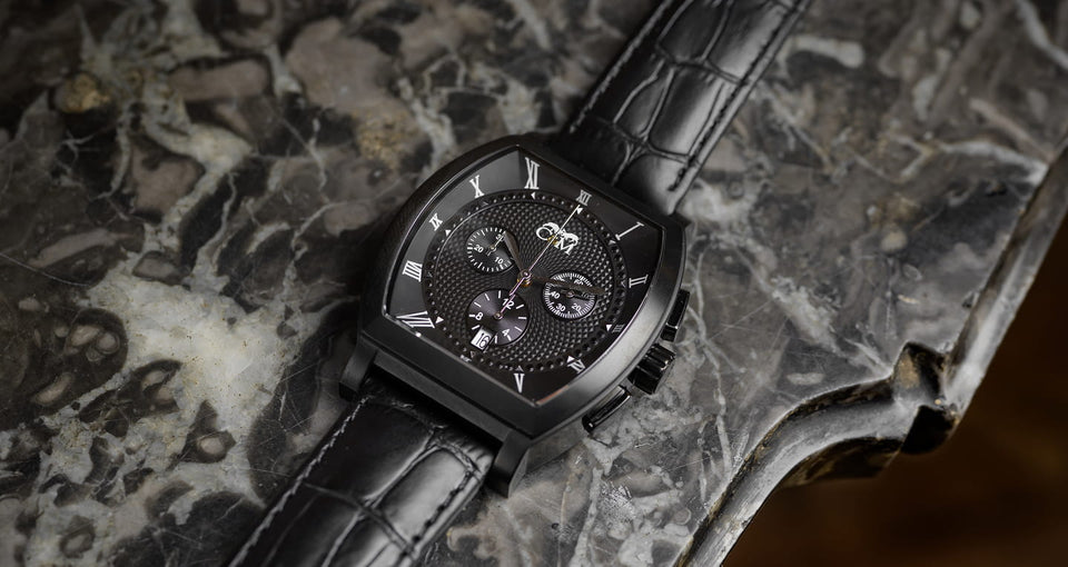 montre tonneau noire chronographe avec bracelet en cuir noir posee sur une table en format horizontal avec mouvement suisse
