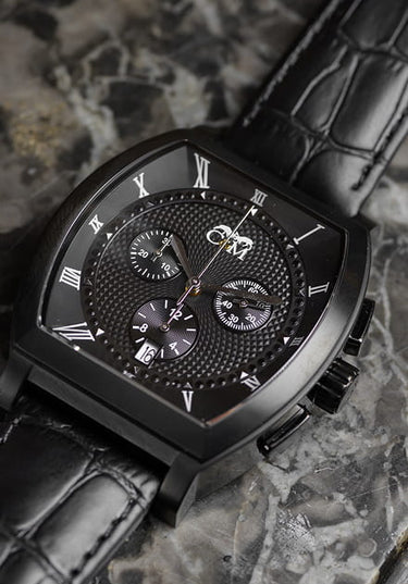 montre tonneau noire chronographe avec bracelet en cuir noir posee sur une table en format vertical avec mouvement suisse